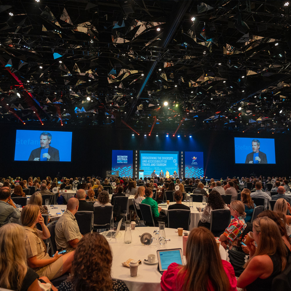 wide view towards a conference stage with many people at circular tables