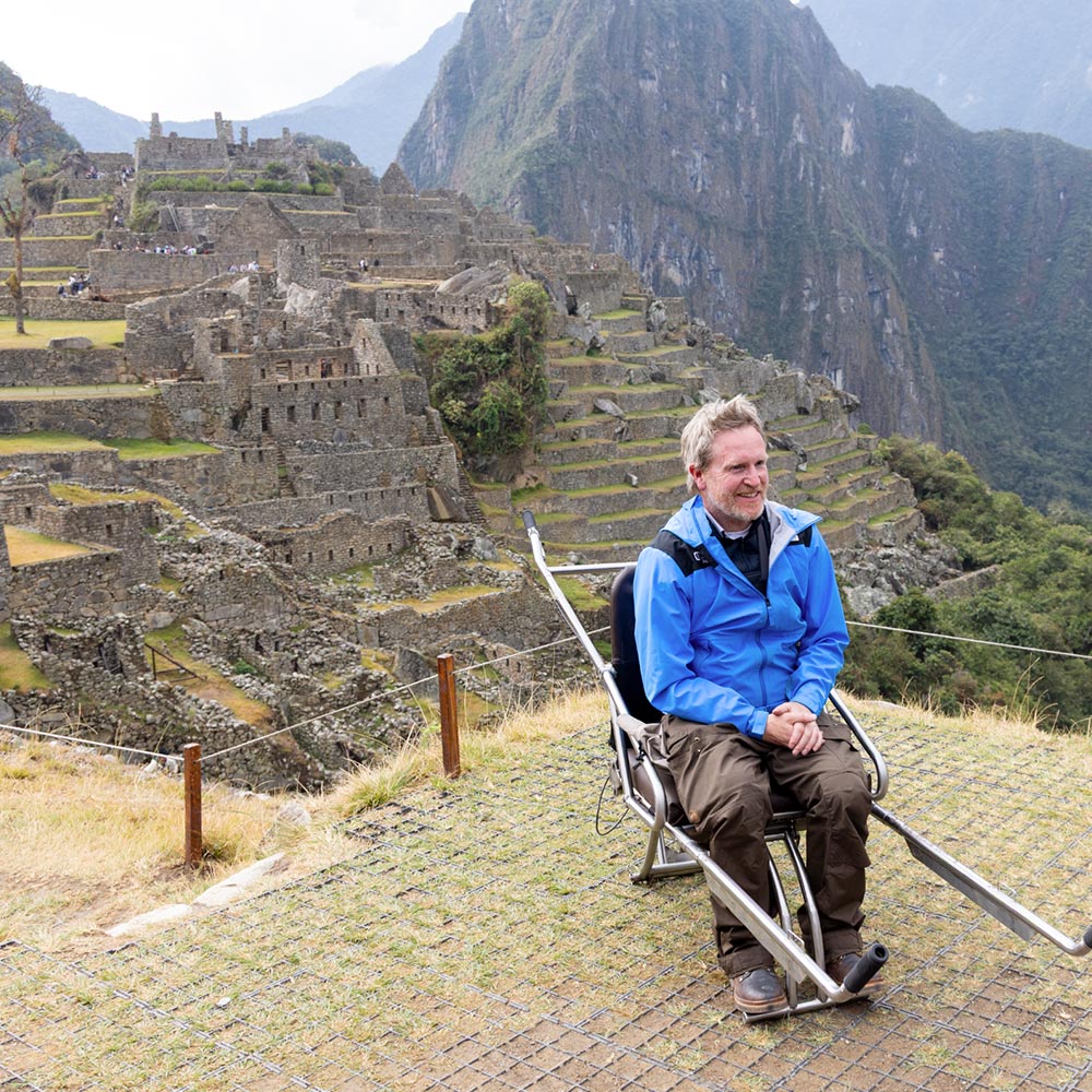 Ryan sitting on a wheelchair with the Machu Picchu mountains and archaeological site in the background