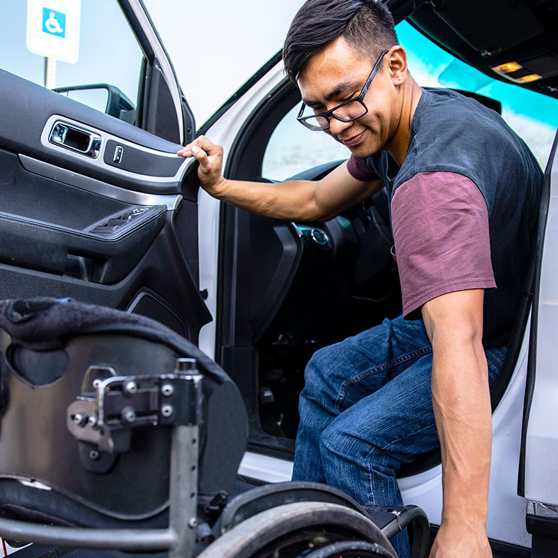 a young asian male driver is transfering from his car onto a manual wheelchair